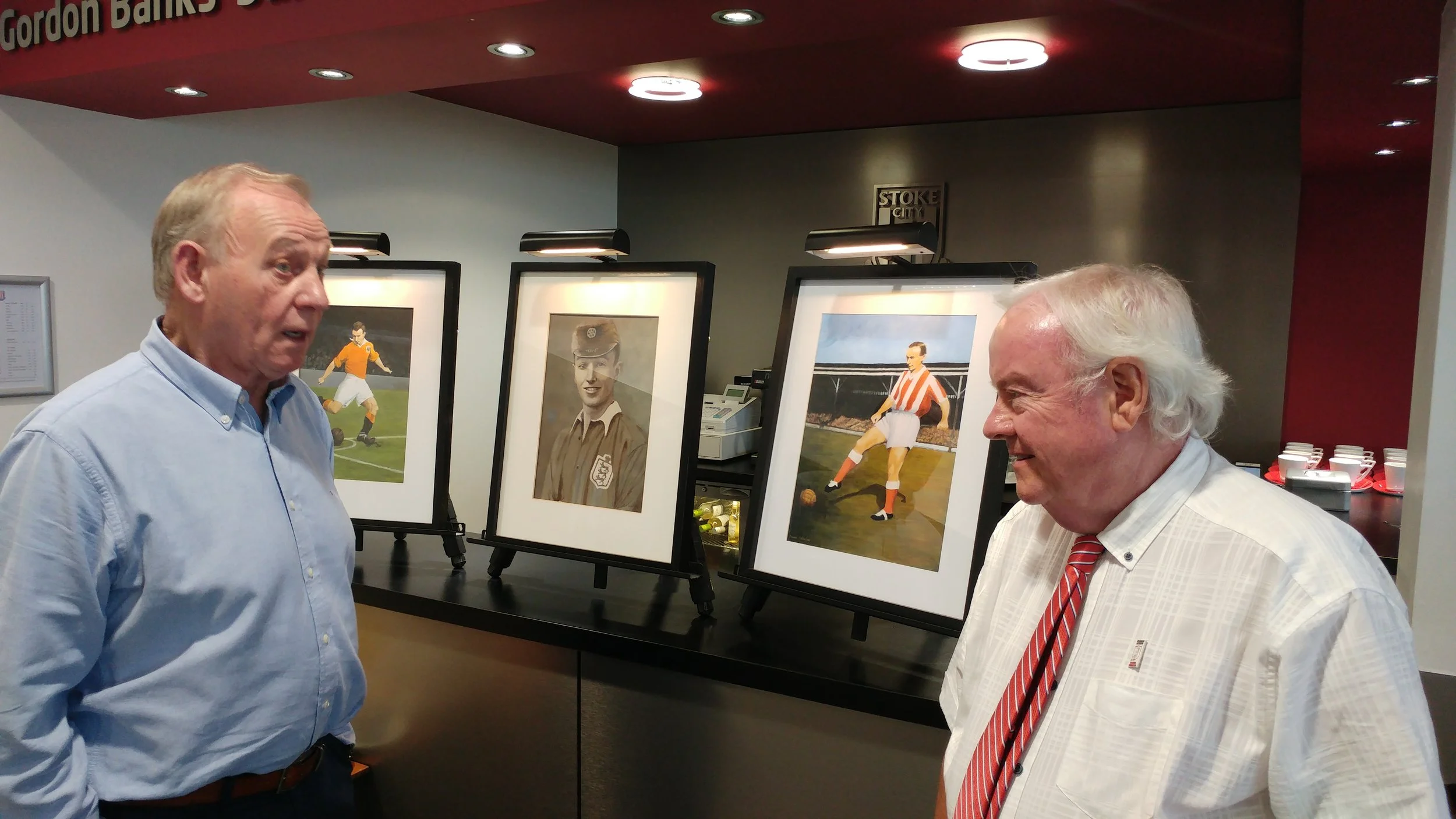 Denis Smith and Roger Horwood in conversation, in front of paintings of Sir Stanley Matthews by local artist Muriel Valentine