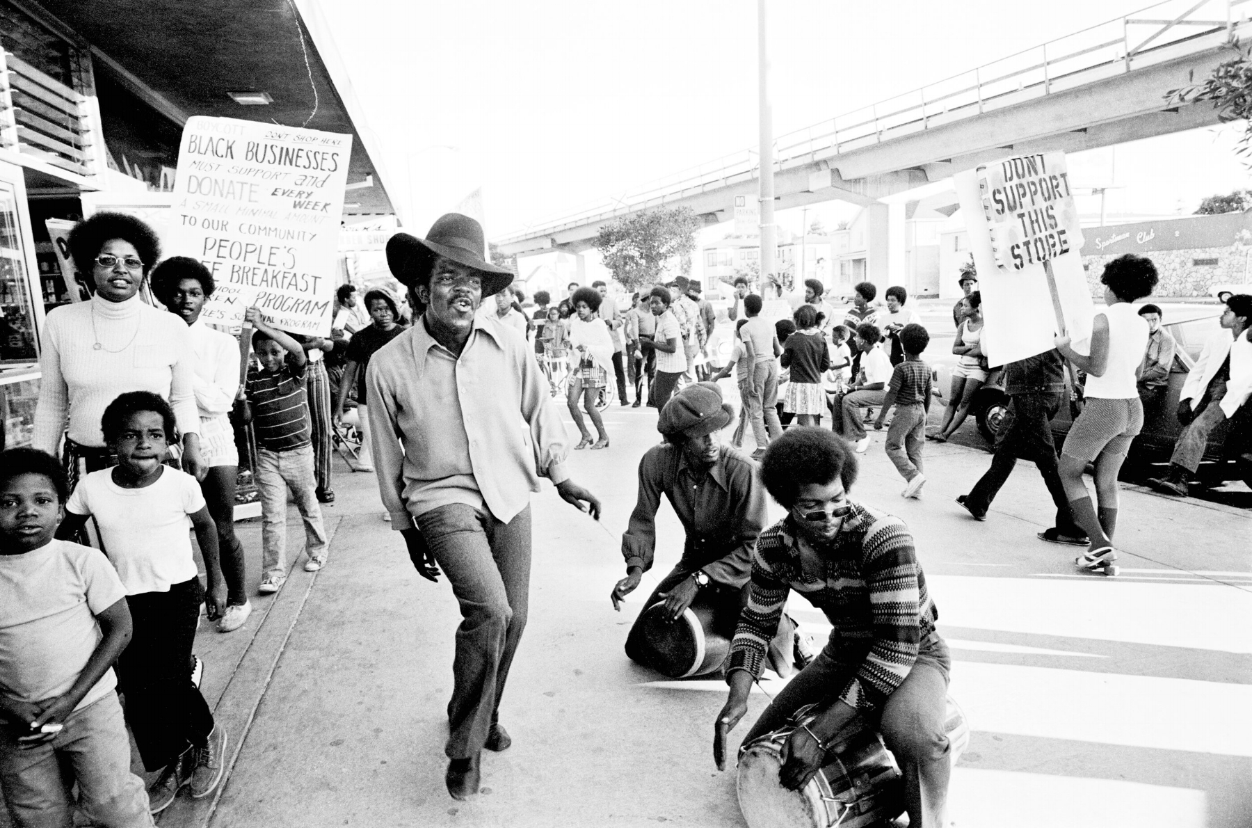 Image Above: The Lumpen, the Panthers’ singing group, performs at the boycott of Bill’s Liquors, Oakland, 1971. Clark Bailey, known as Santa Rita, is dancing. Michael Torrence (front) and James Mott (back) are drumming. All images: Stephen Shames, Courtesy of Steven Kasher Gallery