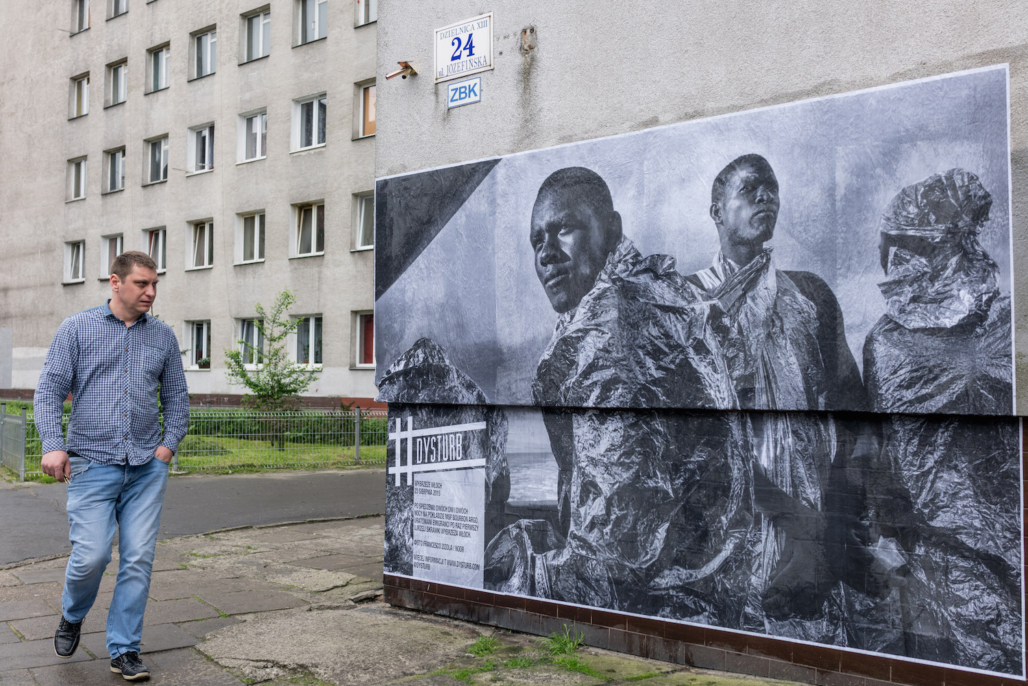 ©Benjamin Girette. For the Krakow Photomonth Festival 2016, we pasted ©Francesco Zizola's (NOOR) photograph at Józefińska 23, 33-332 Kraków, Poland. The caption reads: 23 August 2015 - Italian coast. After spending two days and two nights on the MSF Bourbon Argos, rescued migrants catch sight of the Italian coast for the first time.