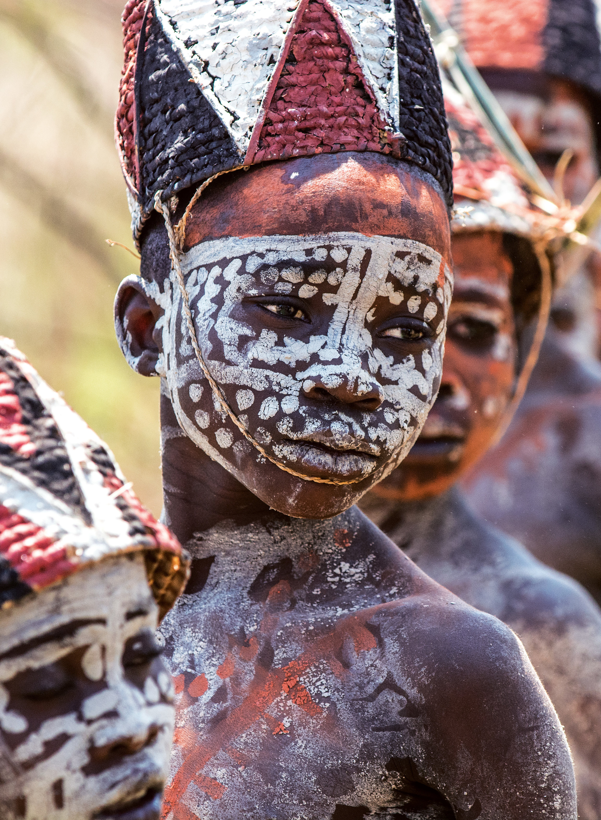 The boys have graduated from their Mukanda initiation, wearing woven hats painted with ocher and charcoal, their bodies covered in chalk. © African Twilight: The Vanishing Cultures and Ceremonies of the African Continent by Carol Beckwith and Angela Fisher, Rizzoli, 2018.