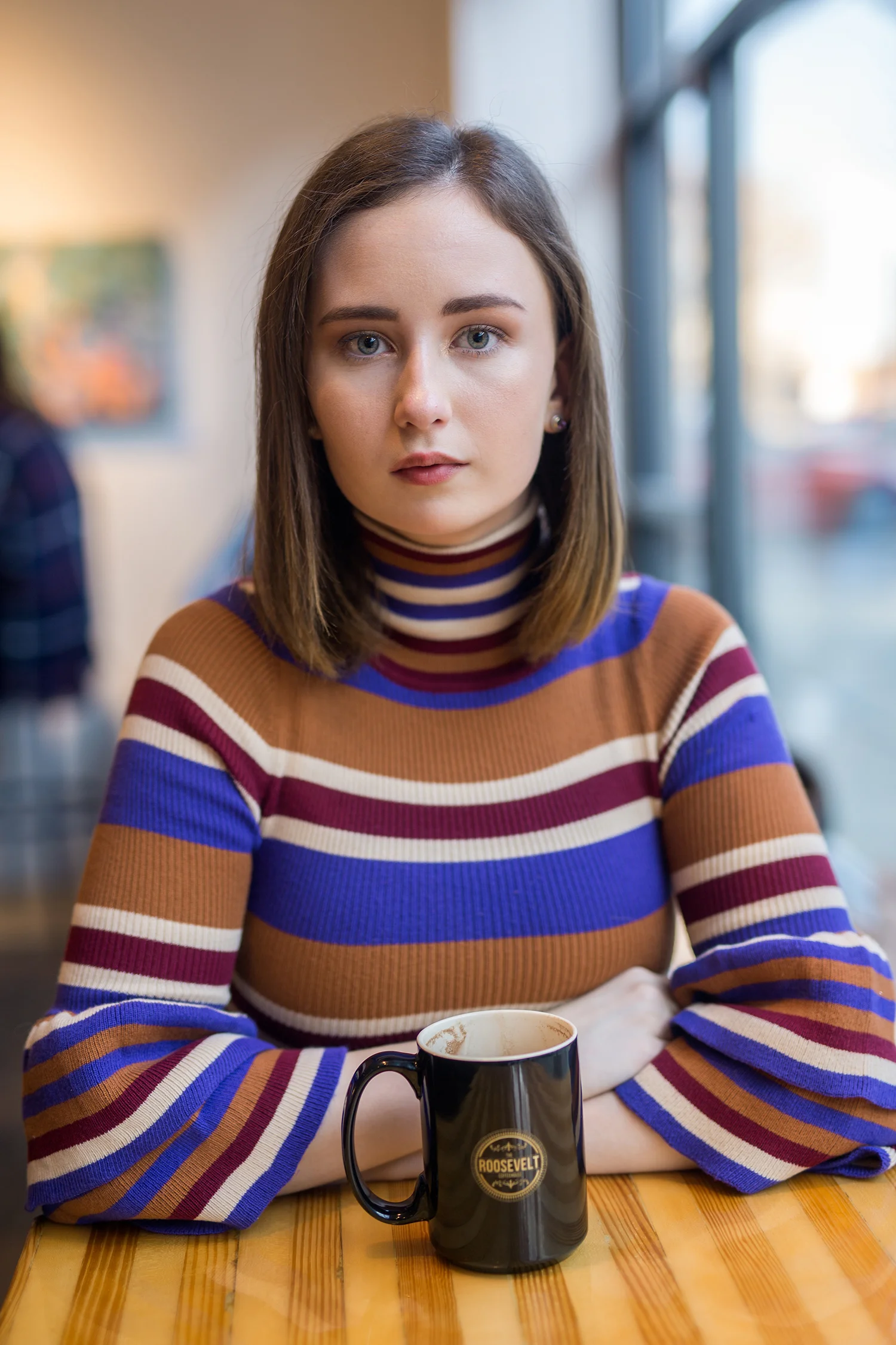 a girl sitting at a table with hot chocolate looking at the camera