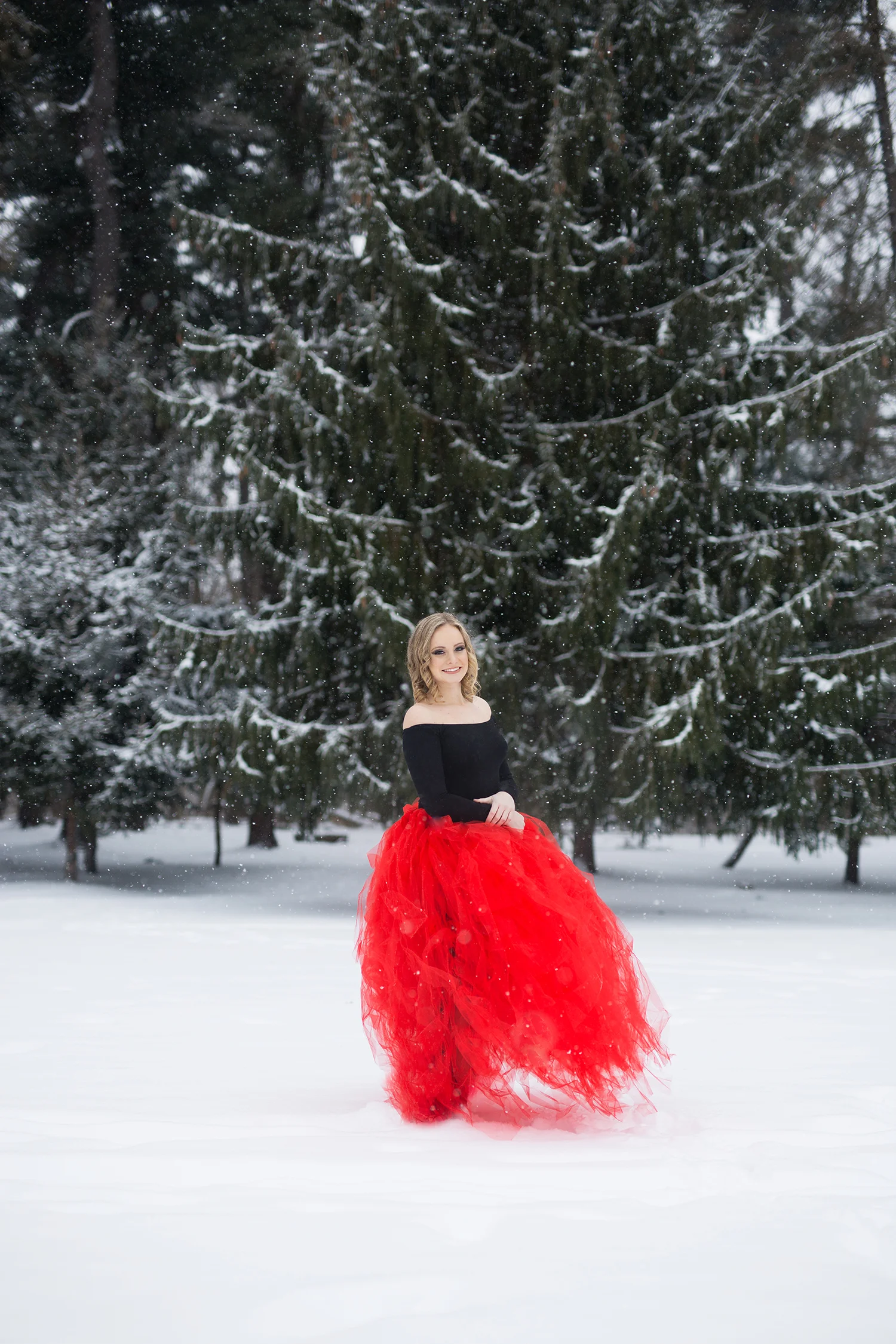 A girl smiling in the snow wearing a red tulle skirt and a black off-the shoulder top.