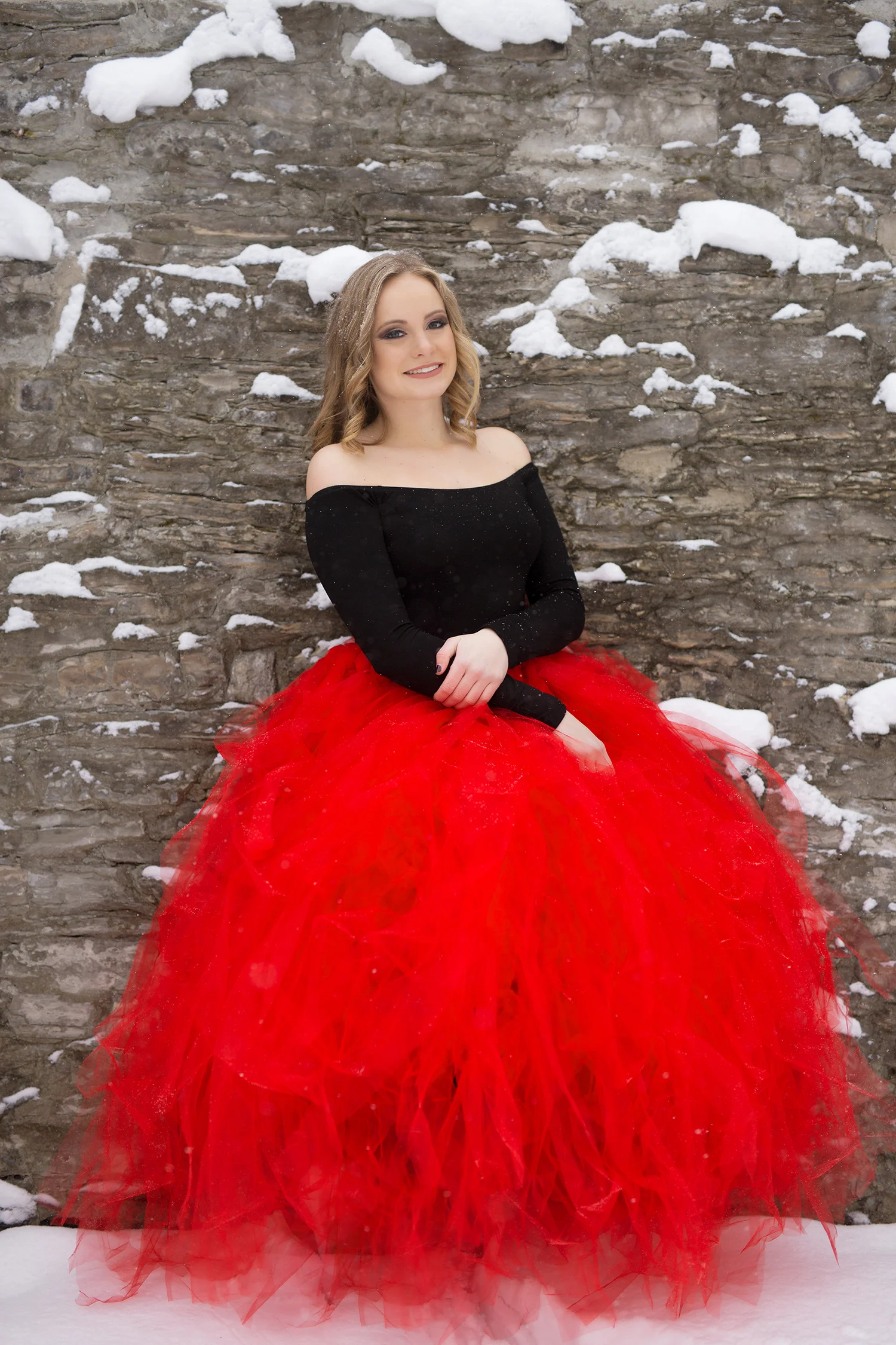 Senior smiling while leaning against a large stone wall.