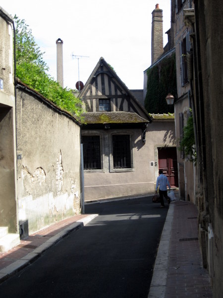 A man carries his shopping home along a narrow street in Auxerre.