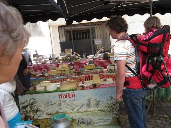 A young father with a toddler on his back contemplates the cheese selection.
