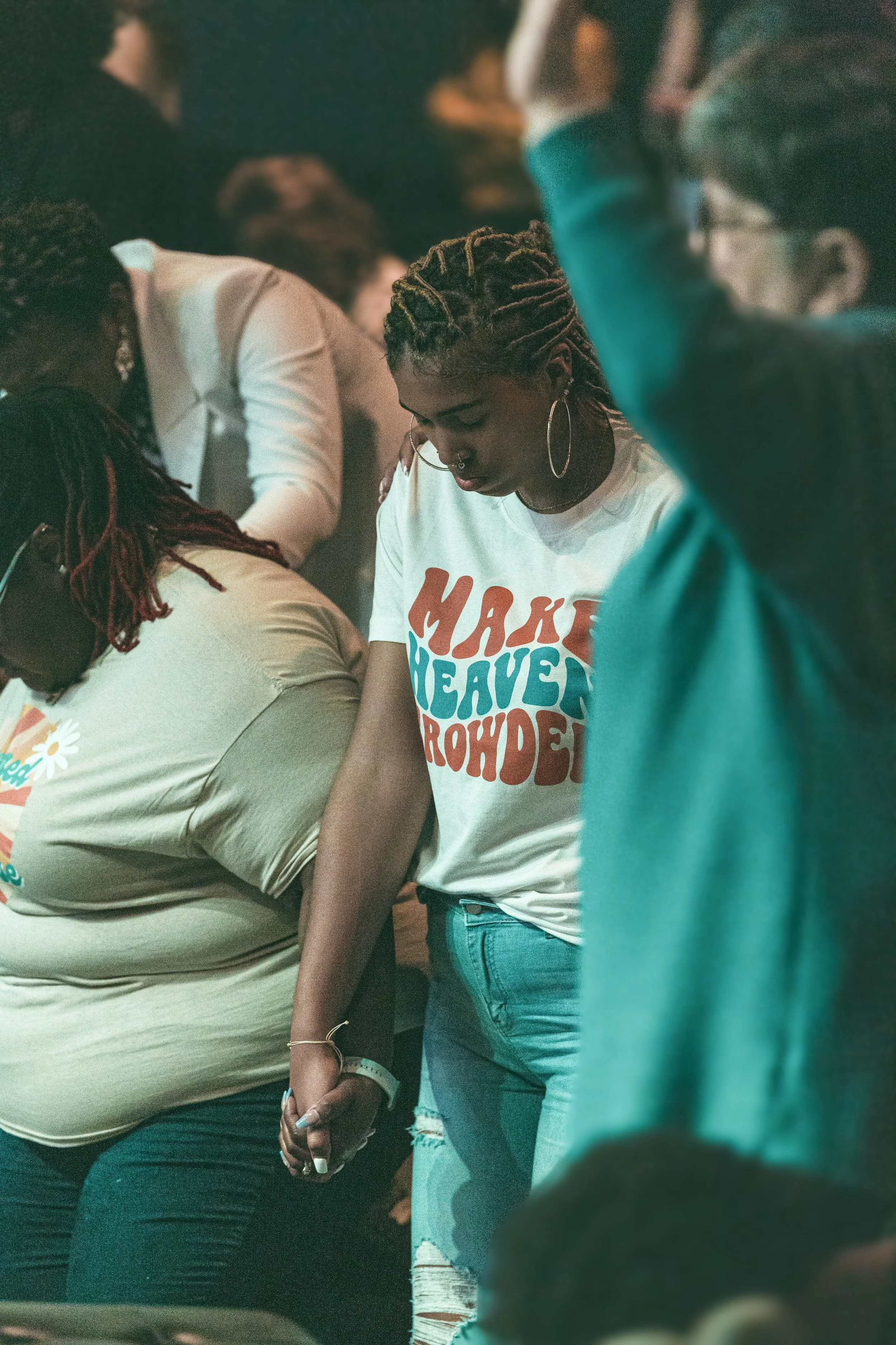 A group of people standing closely together, holding hands and praying, in a solemn setting.