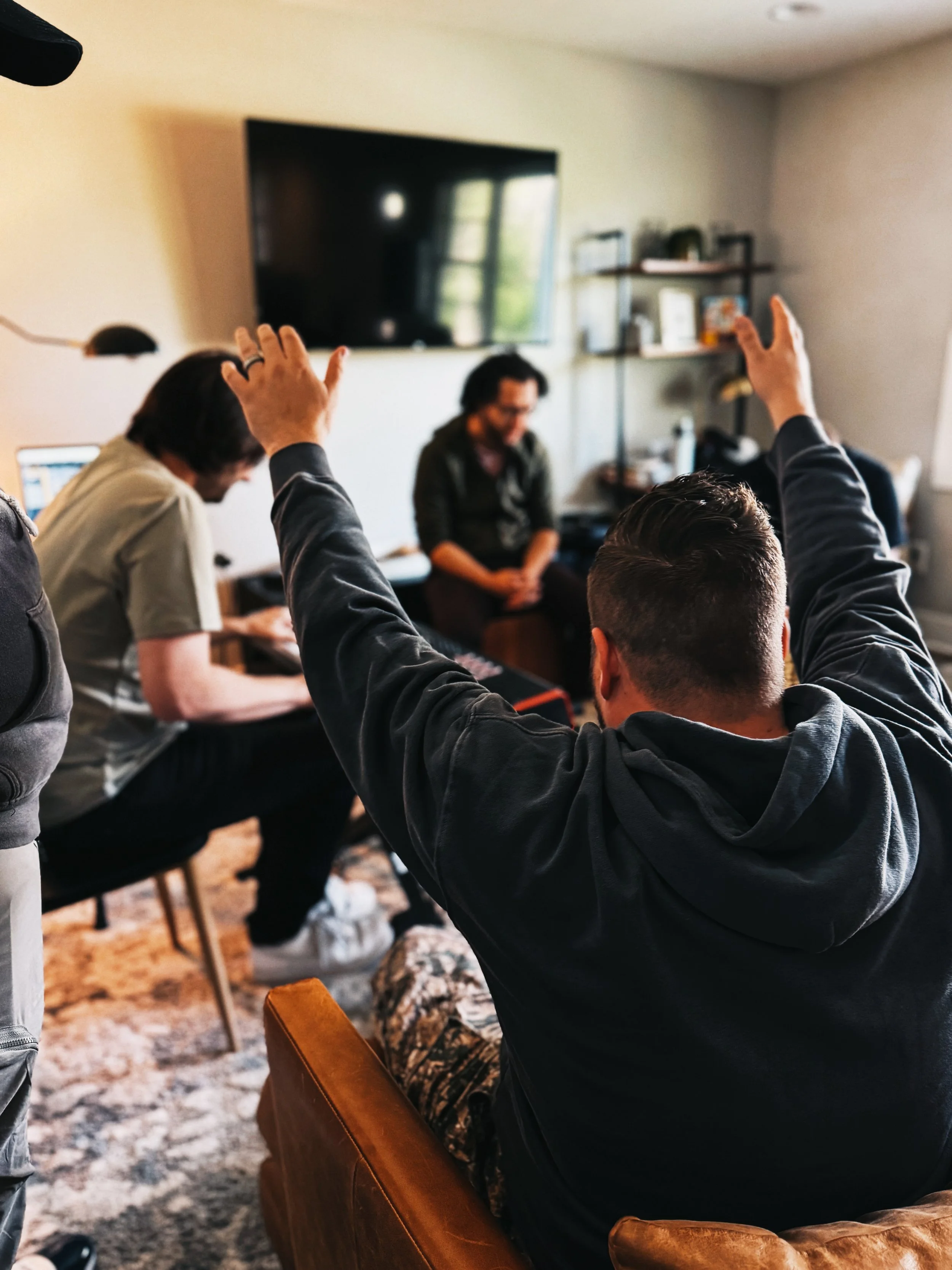 People sitting in a living room during a discussion, with one person raising their hand.