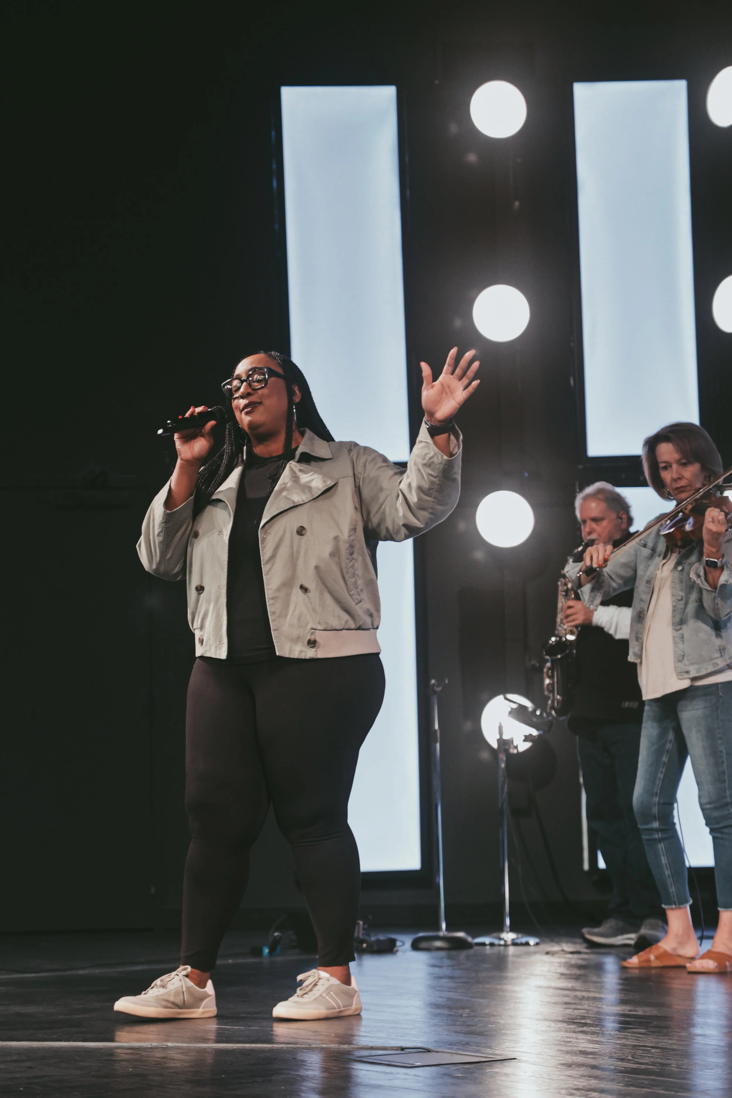 A woman singing into a microphone on stage with a band in the background.