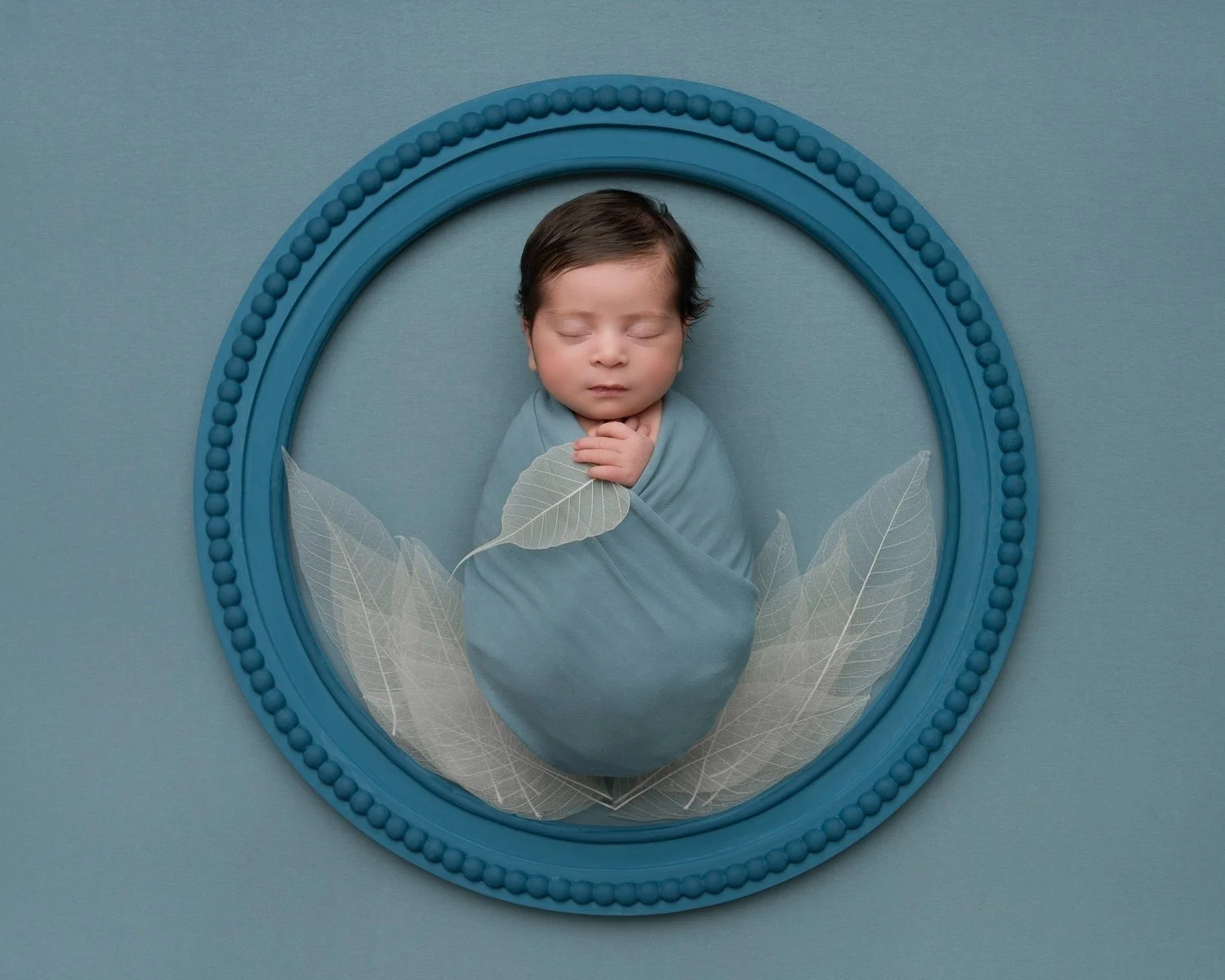 Newborn baby boy asleep inside a blue ring prop during a relaxed newborn photoshoot in Milton Keynes