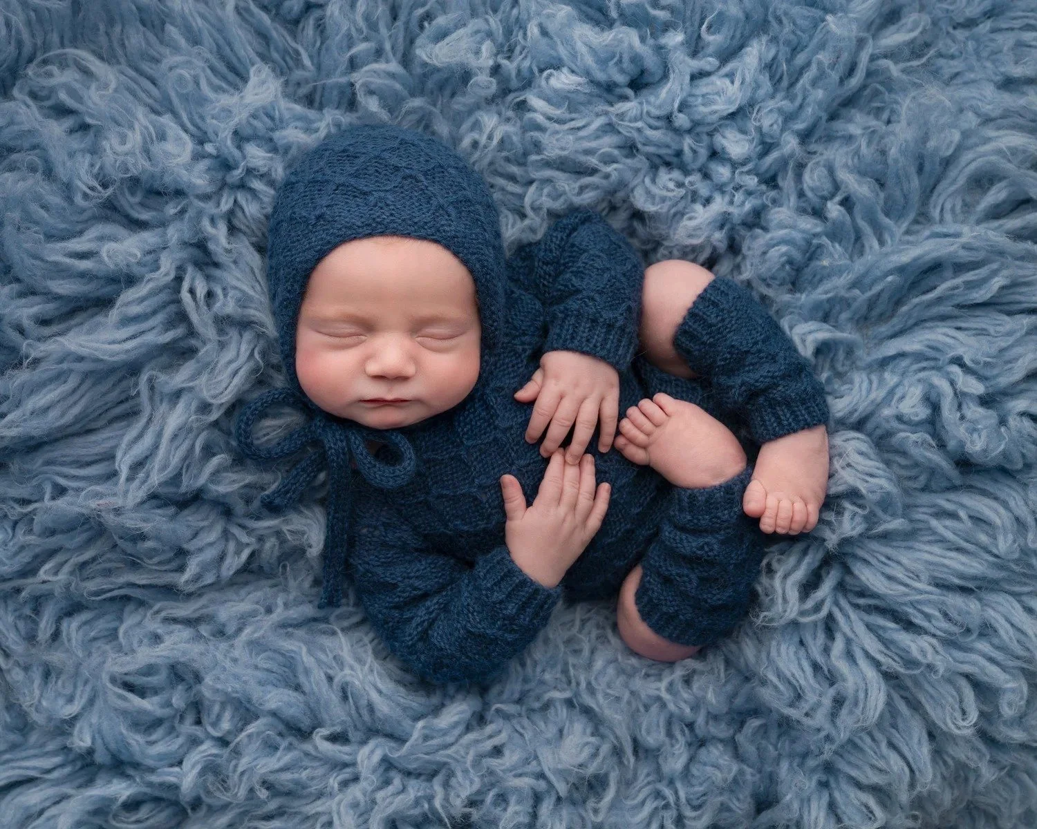 Newborn baby asleep in a navy knitted outfit, newborn photographer Milton Keynes