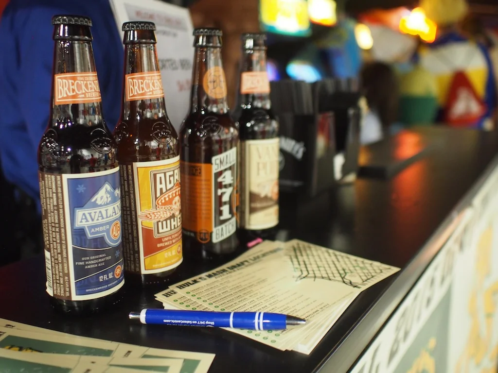 Four bottled beers on a bar counter with a pen and papers in the foreground.