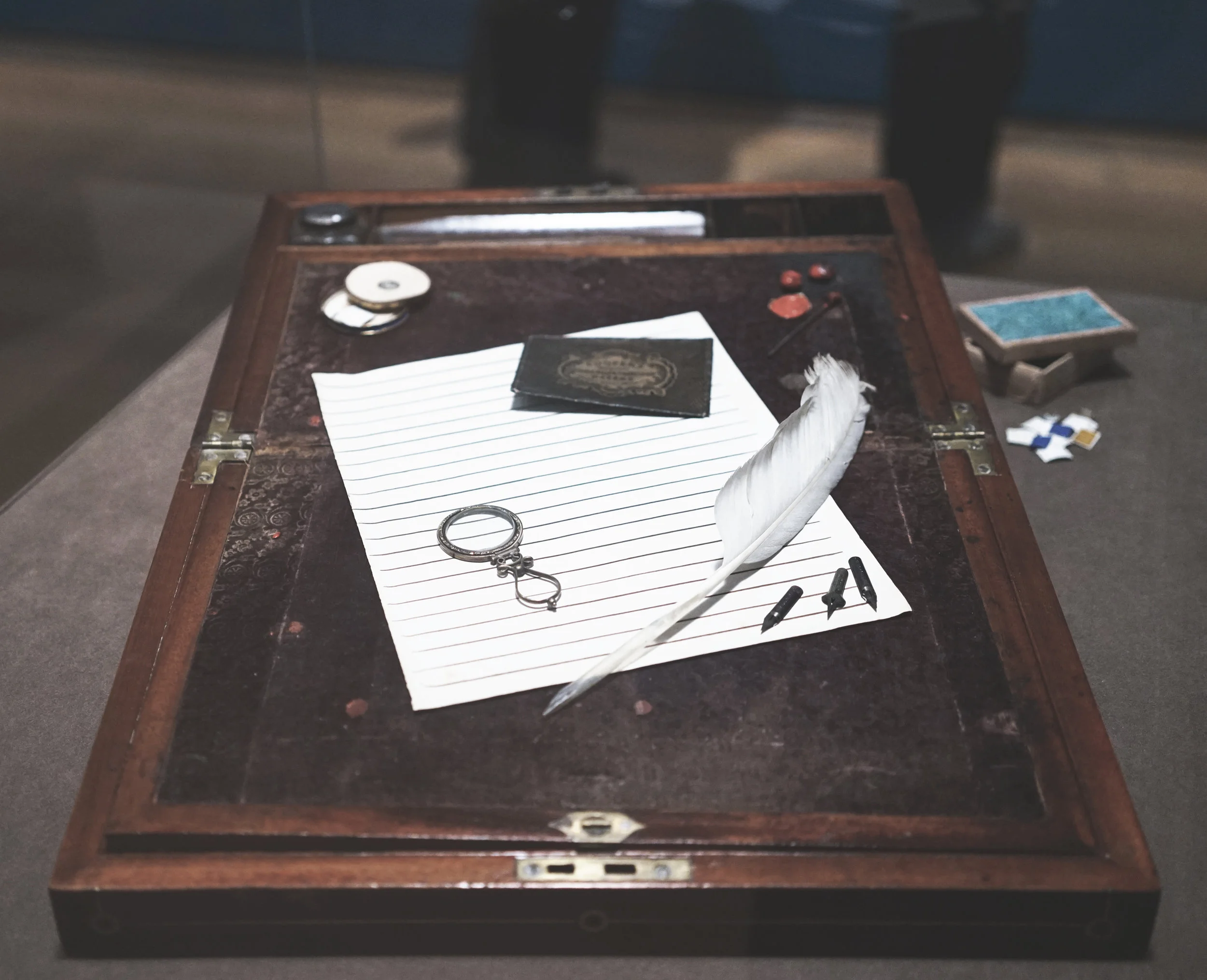Brontë's portable writing desk. Brontë's hinged box opens flat to produce a sloped, velvet-covered surface suitable for writing letter (or composing novels). It was compact enough to set up on the dining room table or pack for use while traveling. Compartments provided storage space for her writing tools, which included inkwells, pen shafts and nibs, sealing wax, and an ivory-handled seal. She kept a plentiful supply of wafers- adhesive discs used as an alternate means of sealing letters. The heavily ruled sheet of paper was a tool for keeping her handwritten lines straight and evenly spaced: she would simply slip it behind her writing paper and follow guidelines.