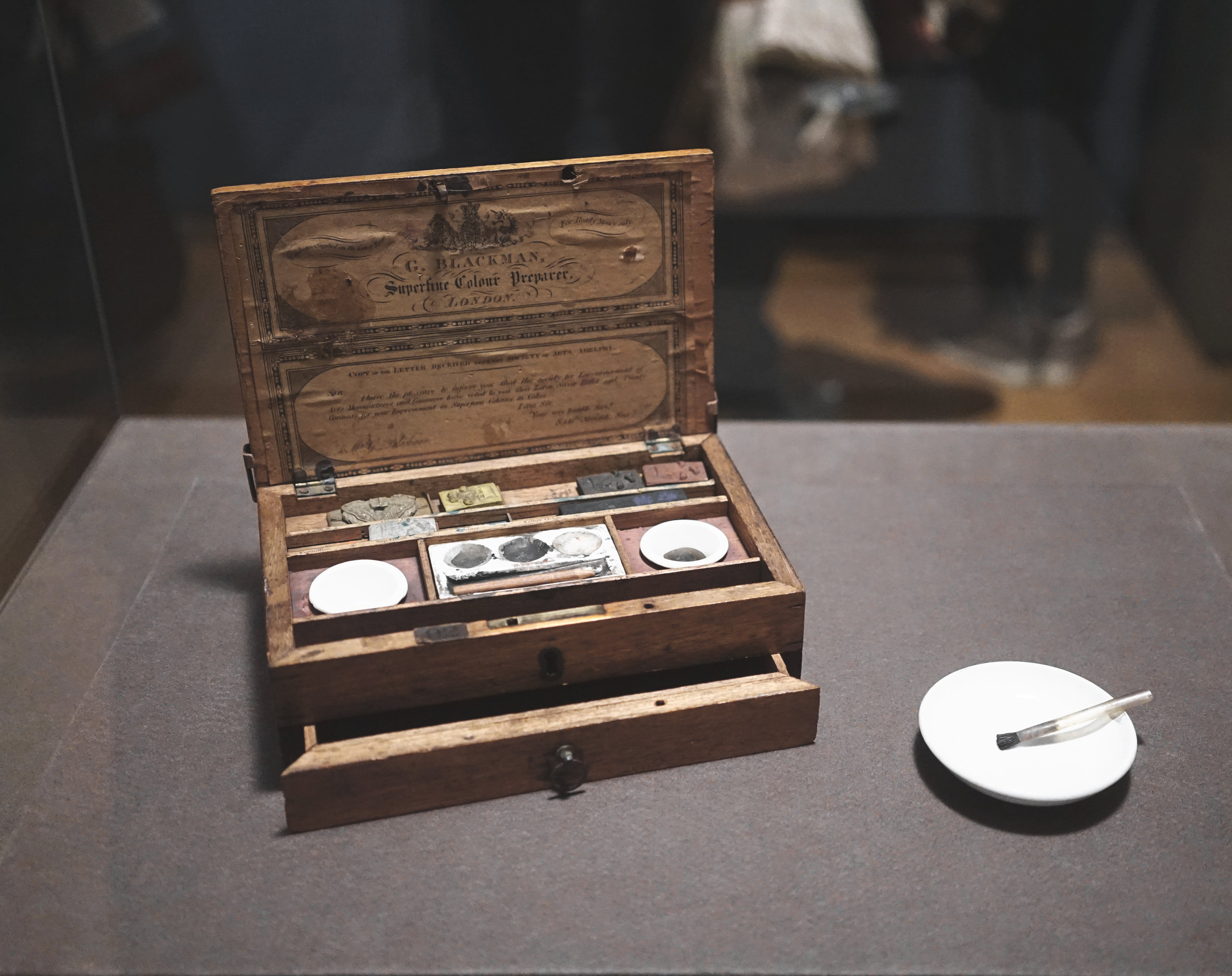 Brontë's Paintbox Brontë filled her portable oak paintbox with the essential tools of a middle-class-amateur artist. It contains twenty-three cakes of soluble watercolor in a variety of hues. To produce paint, Brontë would dip the cake in wake and rub it onto one of the porcelain saucers. One of her hog's-hair brushes is fitted to a quill. The symbol on the unused cakes- three ostrich feathers rising through a coronet- is the heraldic badge of the Prince of Wales and the trademark of the supplier, or colorman, George Blackman. His trade card, which advertises his services as a "Superfine Colour Preparer," is adhered to the inside of the lid along with a copy of testimonial from the Society for the Encouragement of Arts, Manufactures and Commerce (known today as the RSA).