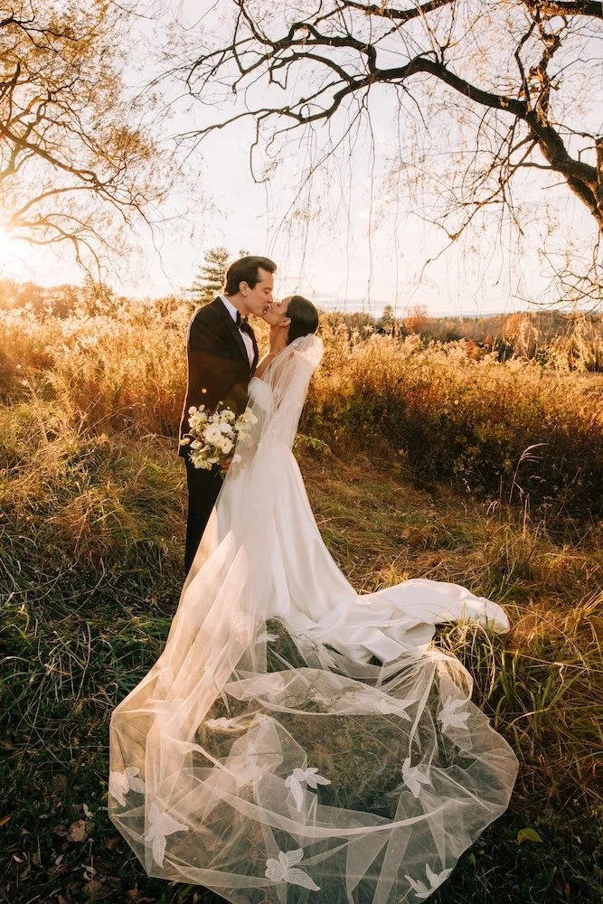 Breathtaking bridal portrait taken during an autumn  sunset of a groom and his bride kissing under two trees.