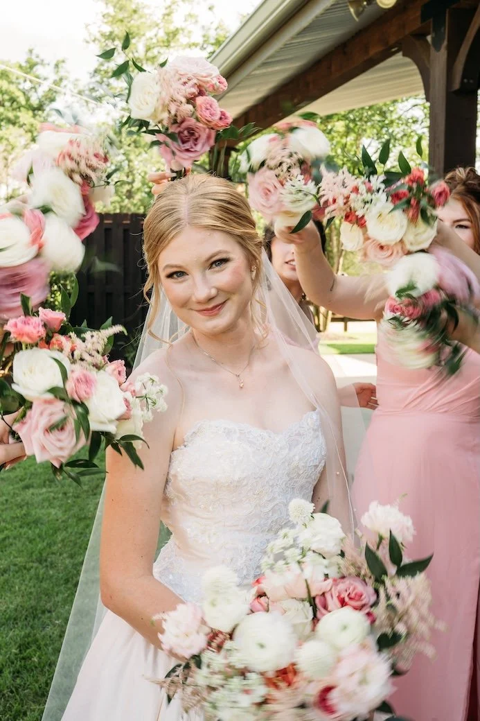 Smiling bride surrounded by pink and white bridesmaid bouquets.