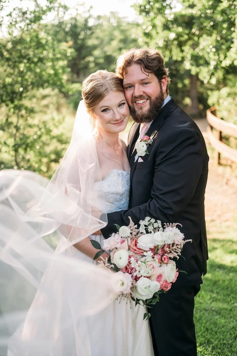 Smiling bride and groom with nuzzled cheeks with cutsom blush wedding veil flowing in the air.