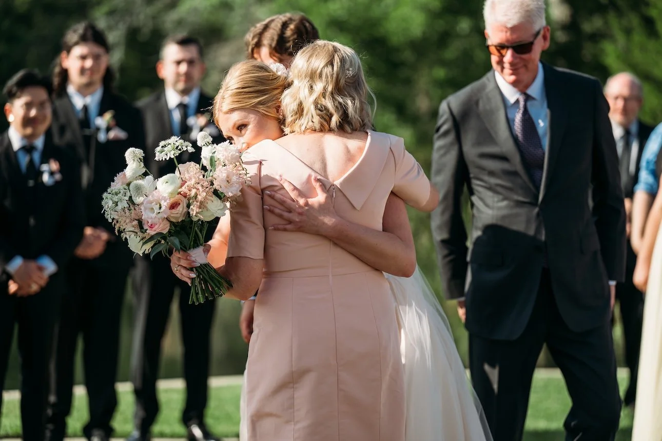 Mom wearing blush gown hugging daughter wearing her restyled blush wedding dress after wedding ceremony.