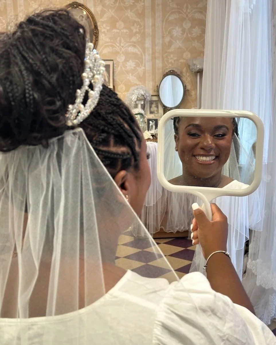 Bride with tight braids looking in a mirror wearing her mom's vintage bridal headpiece.