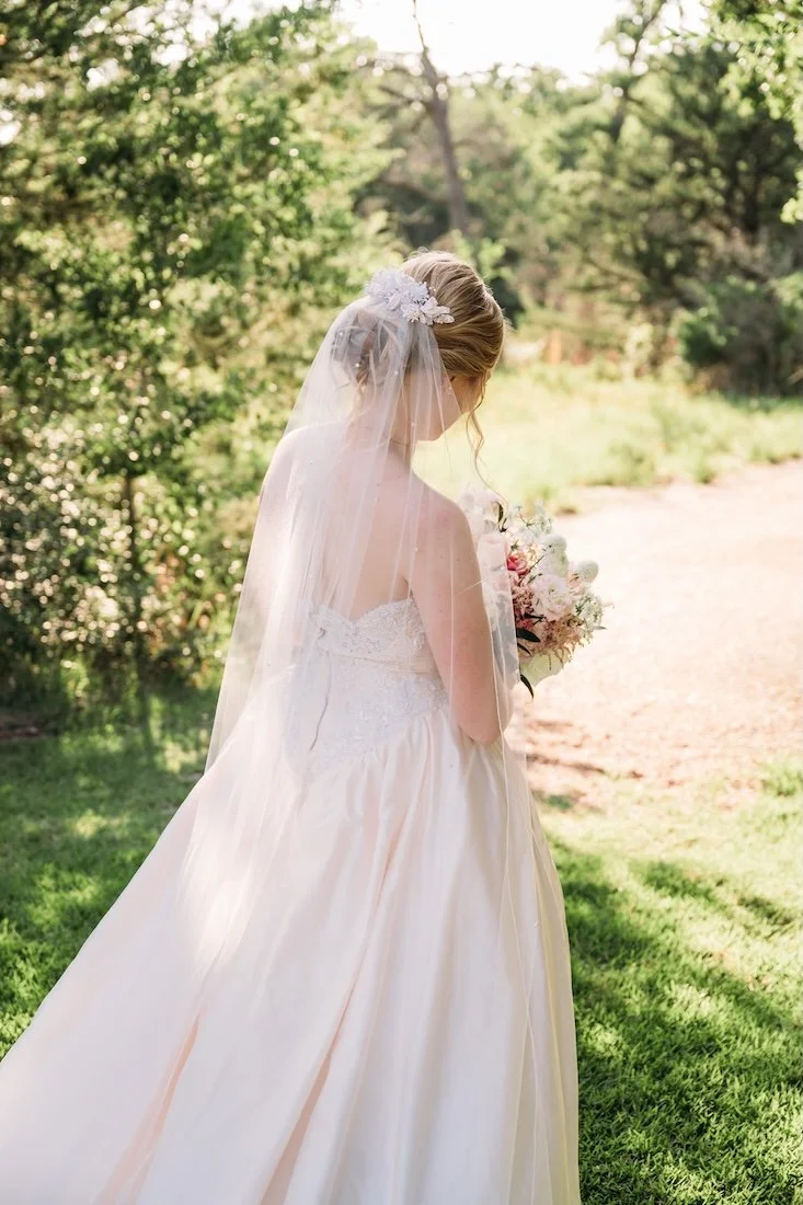 Bride looking down at her bouquet wearing her mom's 90s wedding dress and repurposed vintage headpiece with new blush wedding veil.