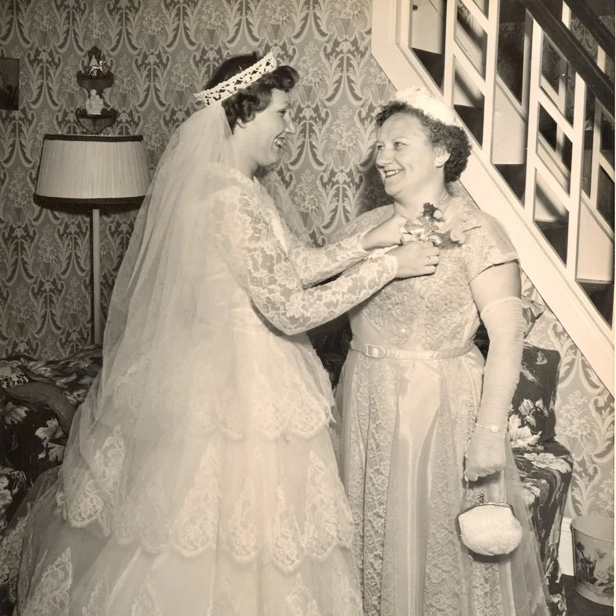 VIntage black and white wedding photo of 50s bride pinning a crosage on her mom.