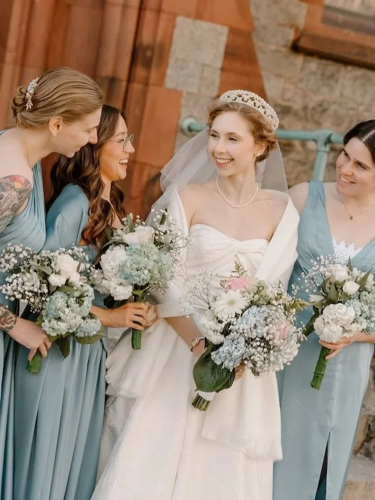 Bride smiling with her three bridesmaids wearing dresses in sea foam blue holding bouquets.