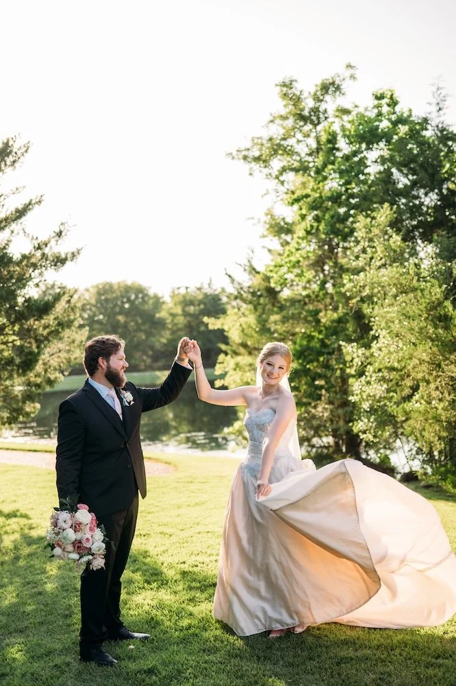 Bride wearing mom's vintage blush wedding dress dancing with groom in the grass.