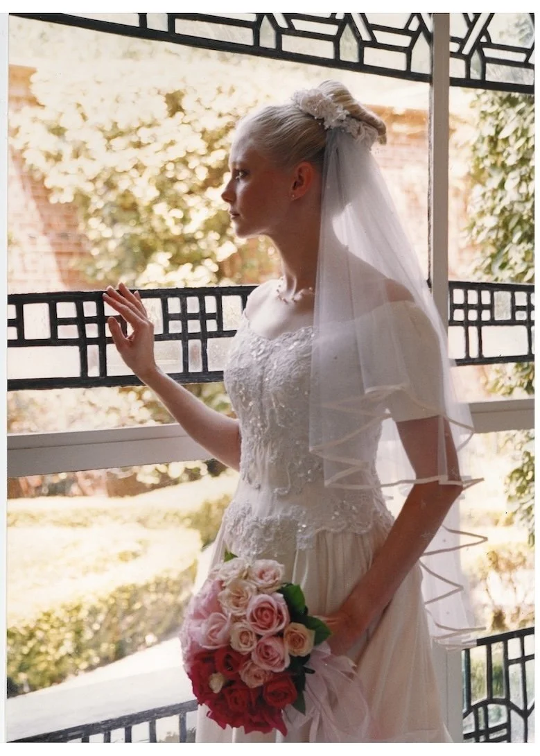 Bride wearing a blush colored gown and wedding veil in 1999 looking out a window.