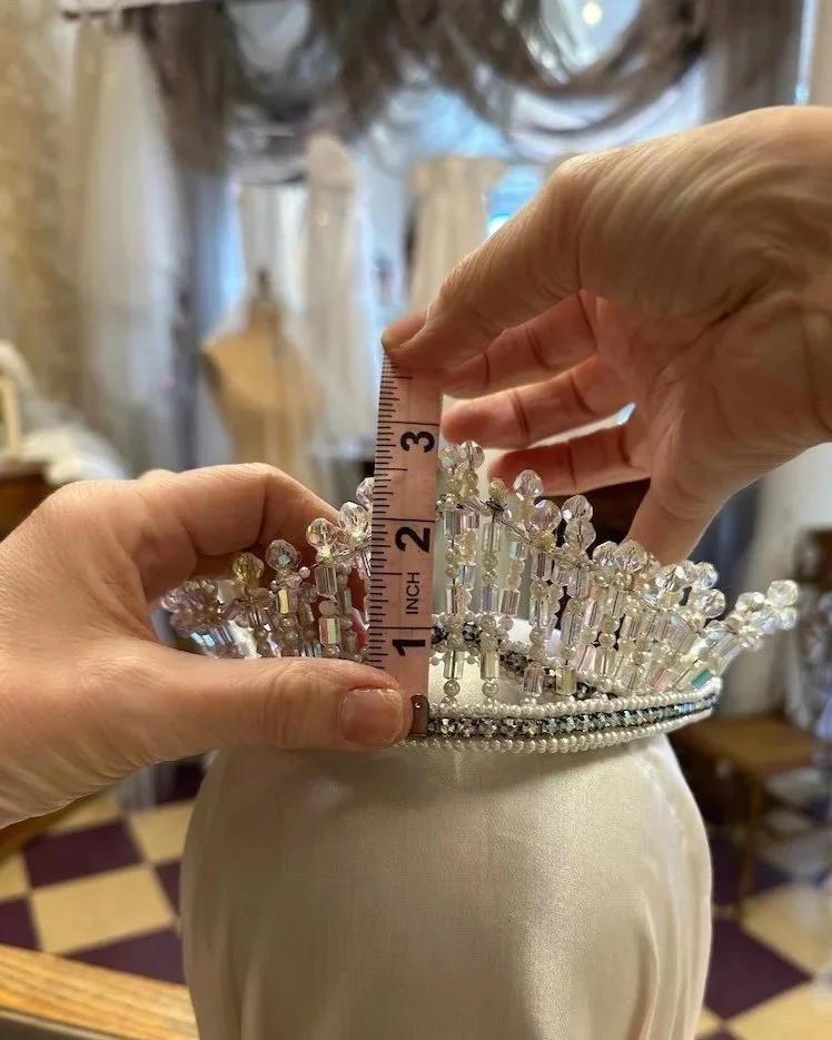 Two hands holding a pink measuring tape showing 3 inch height of grandmother's crystal and pearl 1960 bridal crown.