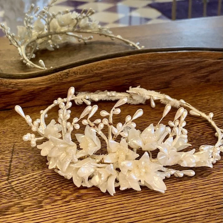 Pristine white wax flower crown displayed on wood shelf at headpiece.com.