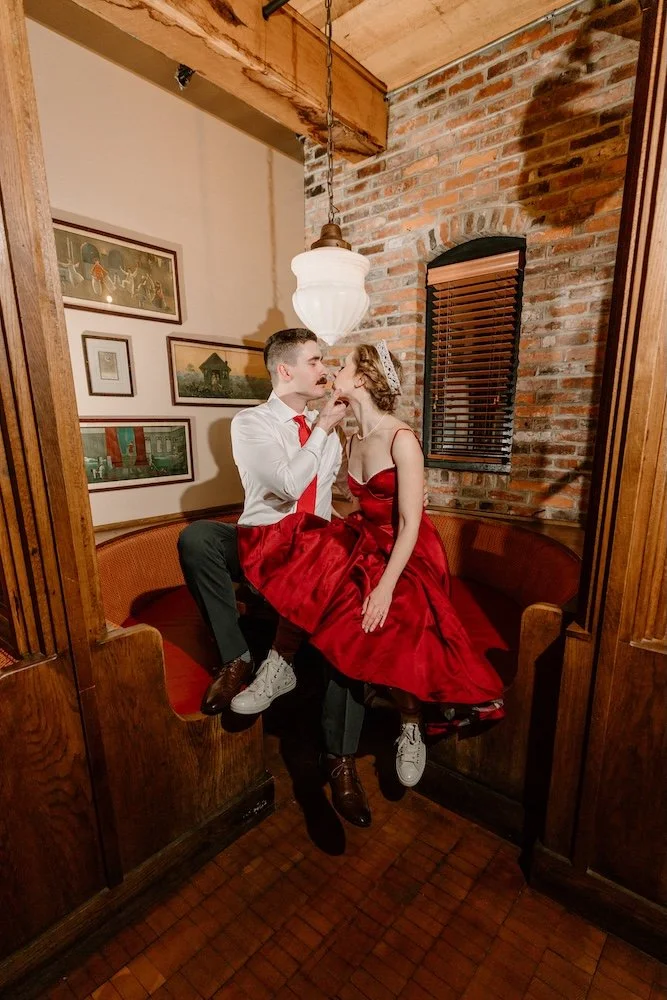 Bride and groom sitting together on top of bar table ready to embrace.