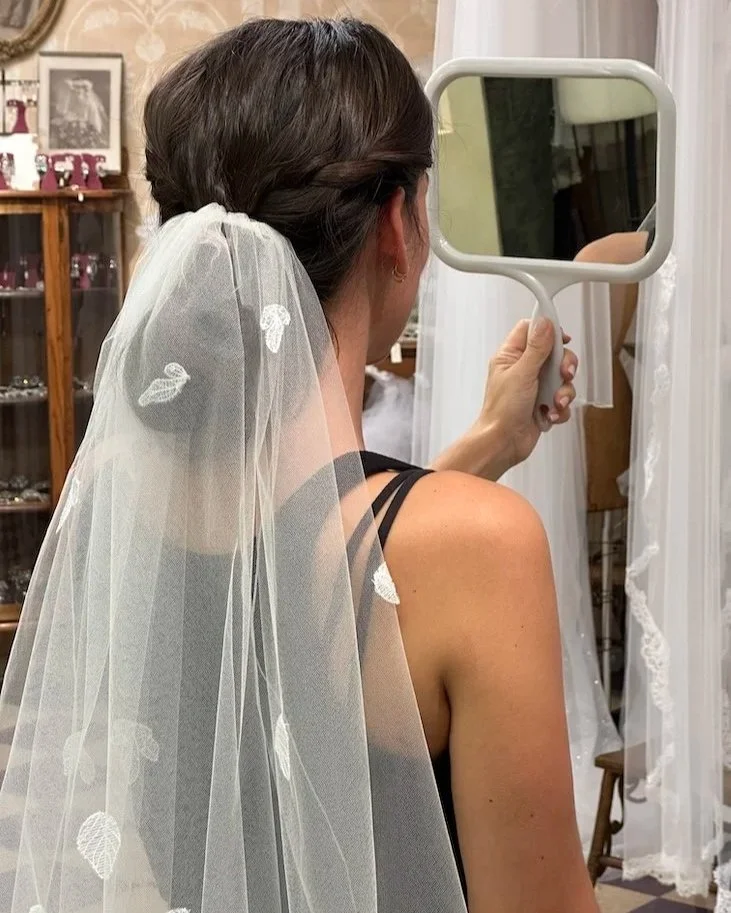 Bride looking in handheld mirror to see the beauty of her custom wedding veil with leaf embroidery.
