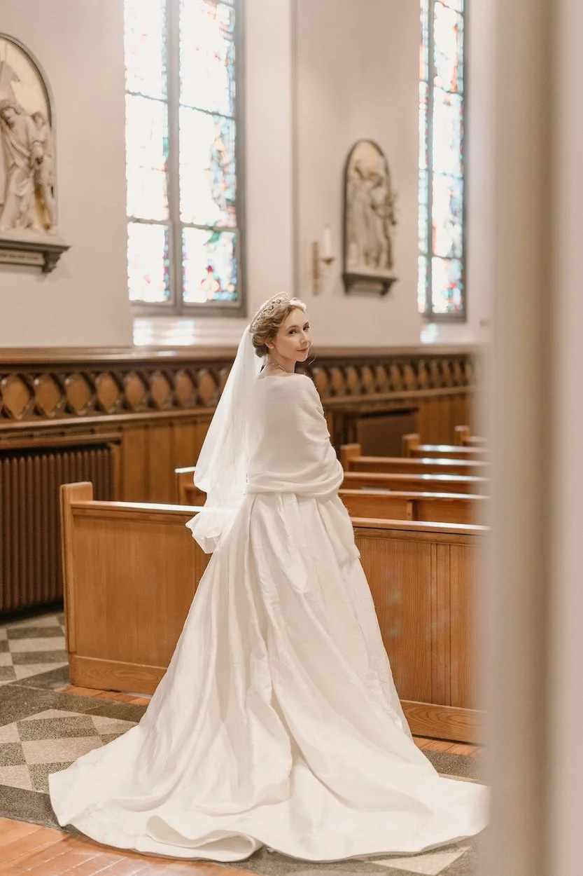 Classic bridal portrait of a bride in church behind rows of pews.