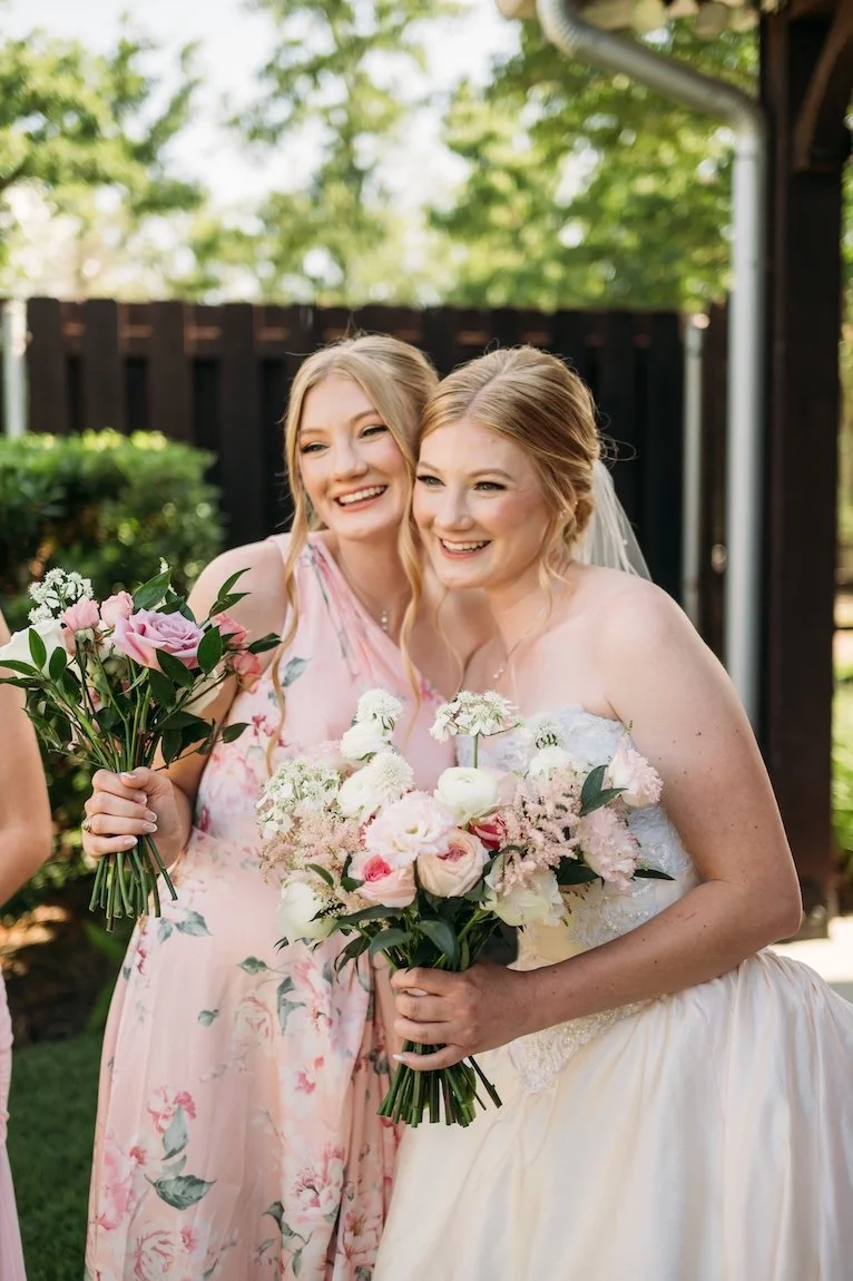 Twin sisters embracing on wedding day wearin blush colored dresses.