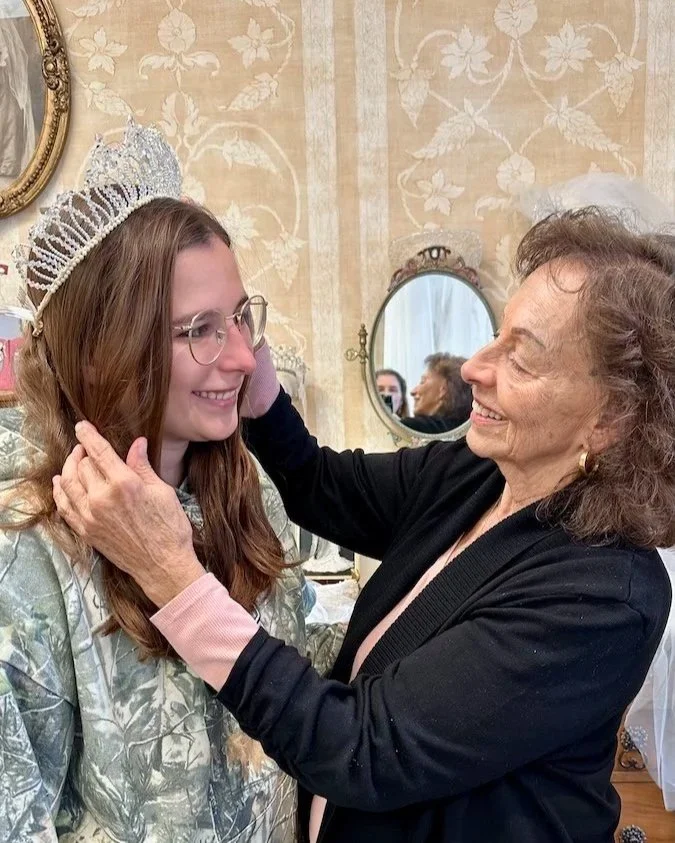 a smiling grandmother trying her 1964 crystal crown on her granddaughter at Headpiece.com.