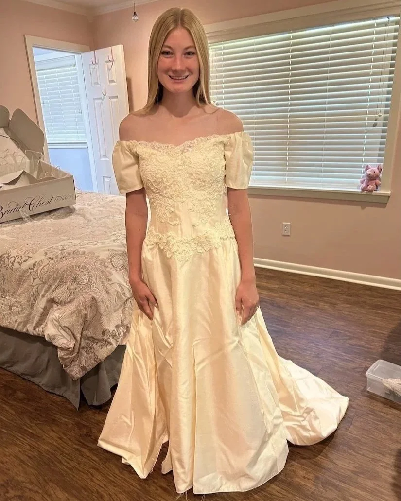 Daughter trying on her mom's 90s blush colored wedding gown in her bedroom.