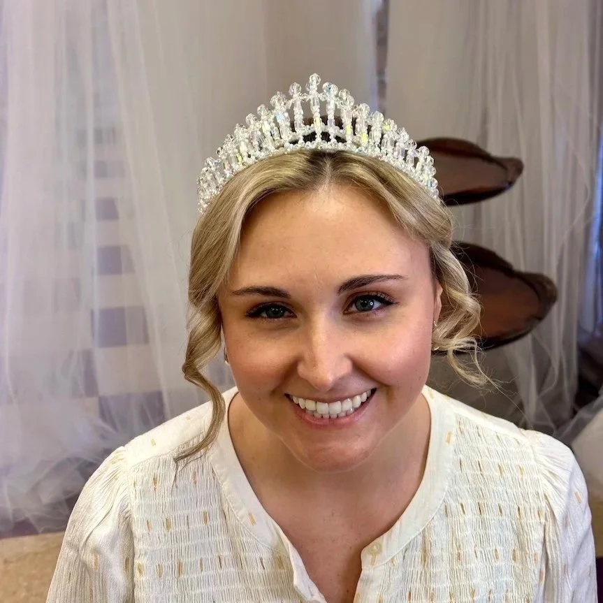Bridal client with blonde hair and blue eyes, smiling while trying on her grandmother's restored vintage crown at Headpiece.com.