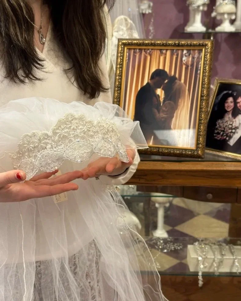 Bride holding mom's 1987 lace headpiece and veil with wedding photos in background