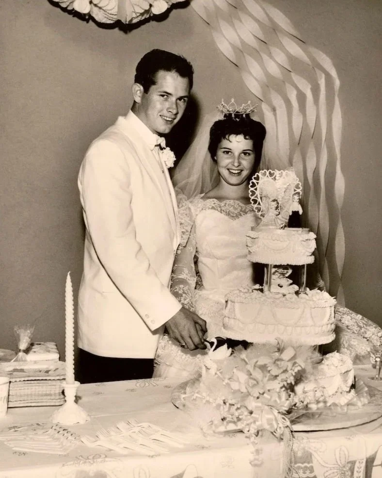 60s Bride wesring gorgeous wedding crown while cutting three tier cake with groom.