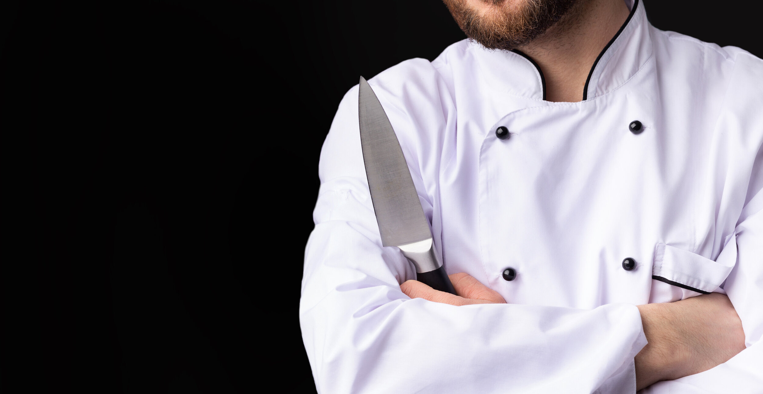 Unrecognizable-Chef-Holding-Knife-Standing-On-Black-Background,-Cropped,-Panorama-1206010040_5639x2916.jpeg