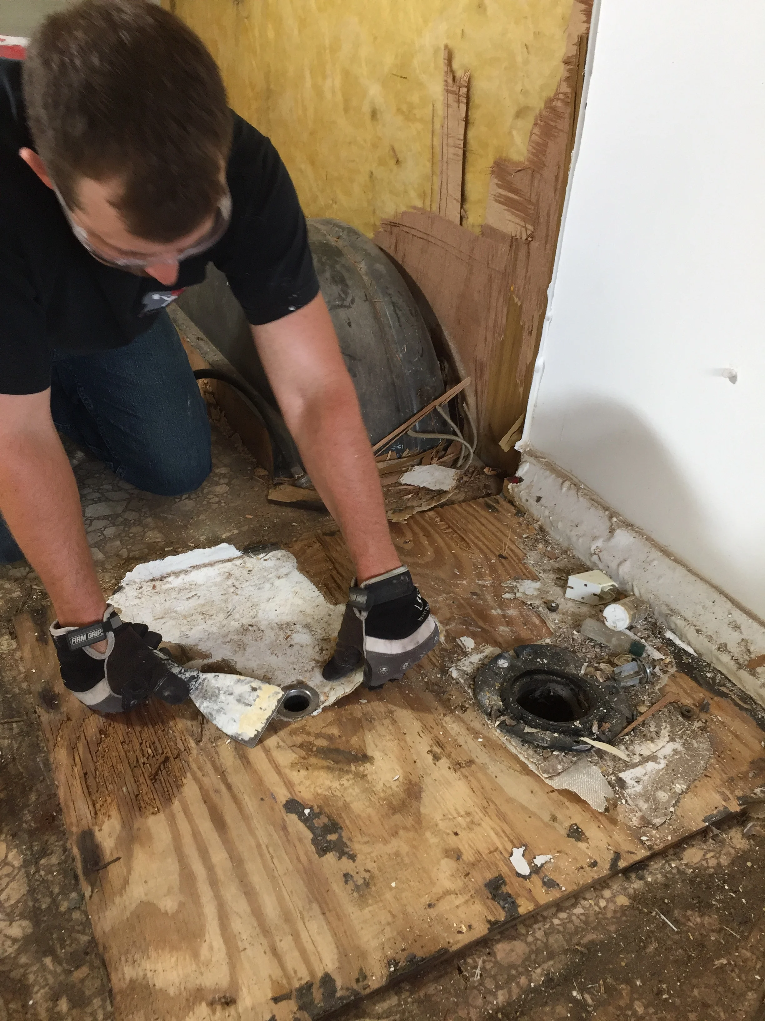 Scraping and chipping off the waterproof, fiberglass coating bit by bit to uncover the screws and rotted shower floor.