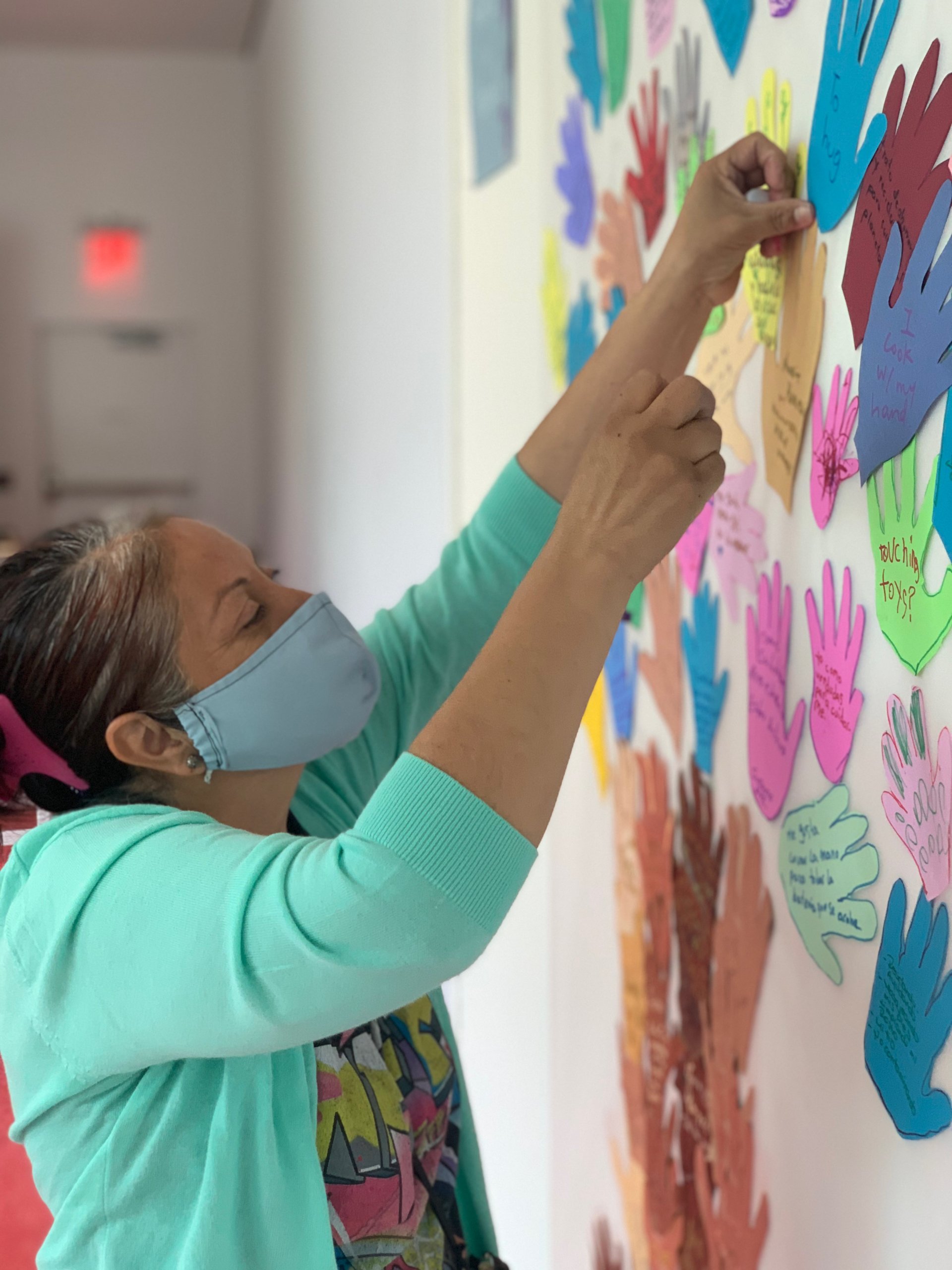 Workshop participant attaching tree of colorful cut out hand shapes from paper onto wall