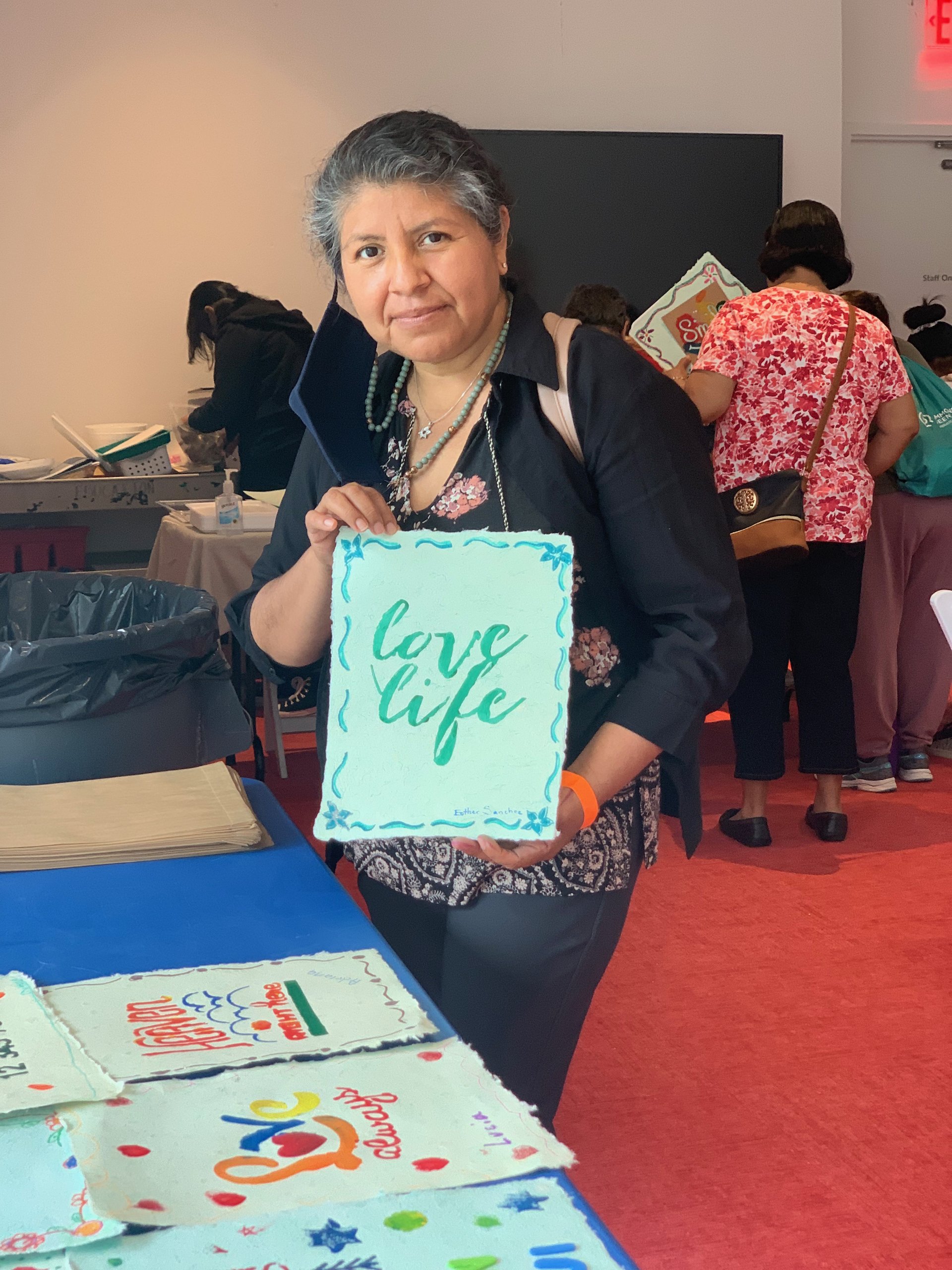 Workshop participant standing at table, holding stenciled print on paper that reads "love life"