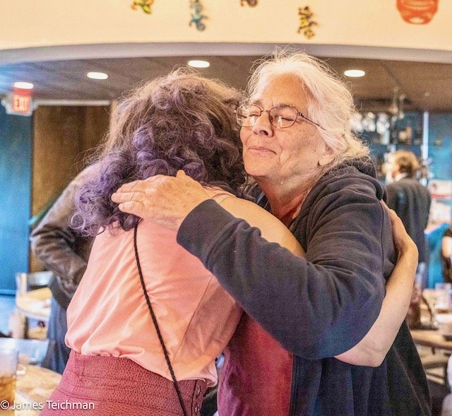  Rachel Heberling hugs an attendee, her back faced to the camera while the other woman's face is expressing contentment. 