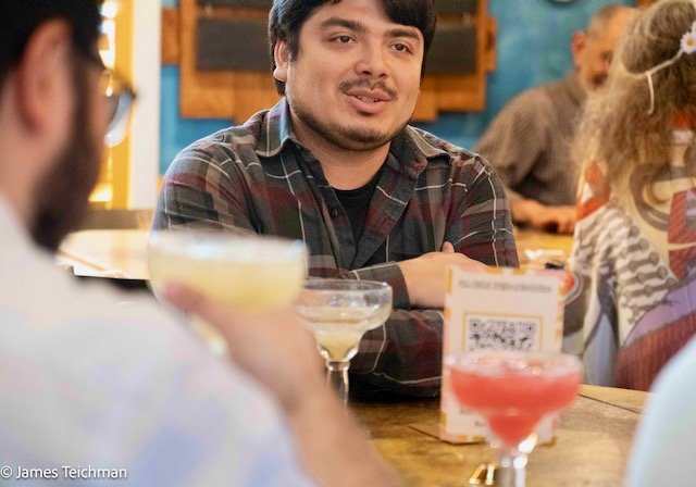  Staff Member Hugo Gatica sits at a table with family and drinks as he's photographed in discussion. 
