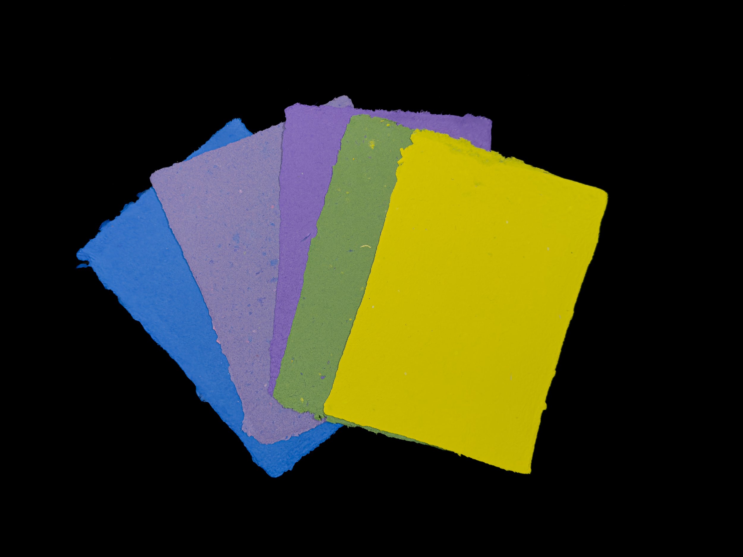 5 sheets of handmade paper on a black background. One sheet is blue, two are shades of purple, one green, and one yellow.