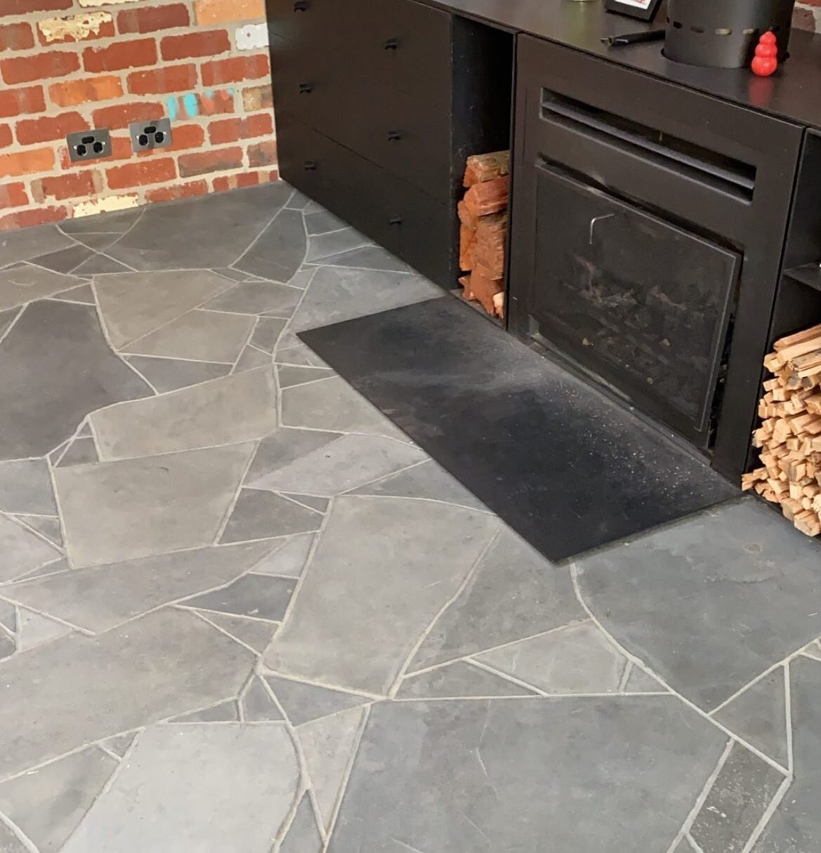 Mintaro slate crazy paving blending in beautifully with the fireplace and recycled red brick wall.
7mm grout joints meant nearly every side of each piece had to be manufactured.

Builder - @built.by.guild 
Crazy paving - @easternlandscapes