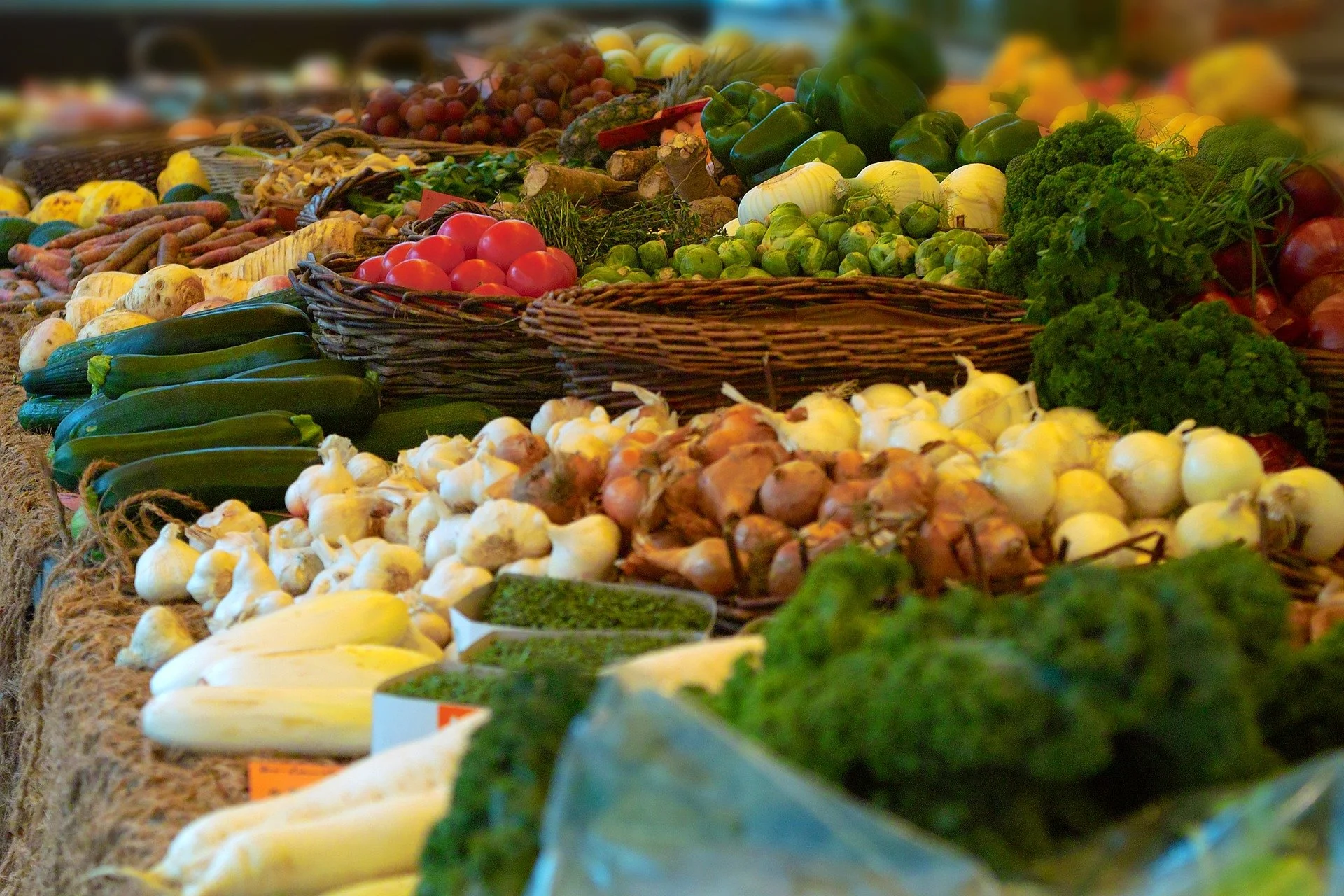 Fresh vegetables and fruits displayed at a market stall, including cucumbers, onions, tomatoes, broccoli, and grapes.