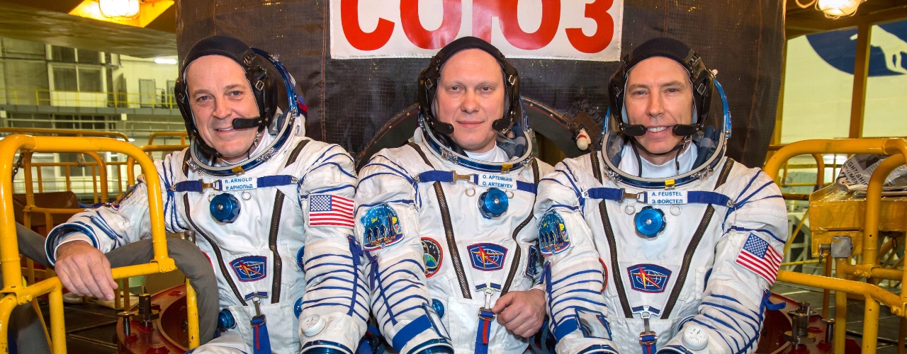 NASA astronaut Ricky Arnold, left, Russian cosmonaut Oleg Artemyev, center, and NASA astronaut Drew Feustel, pose for pictures in front of their Soyuz MS-08 spacecraft during vehicle fit checks in March 2018. Credit: NASA/Victor Zelentsov