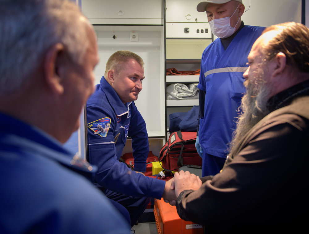  A Russian Orthodox Priest welcomes Aleksey Ovchinin’s hand after the Soyuz MS-10 in-flight launch abort. Credit: NASA/Bill Ingalls 