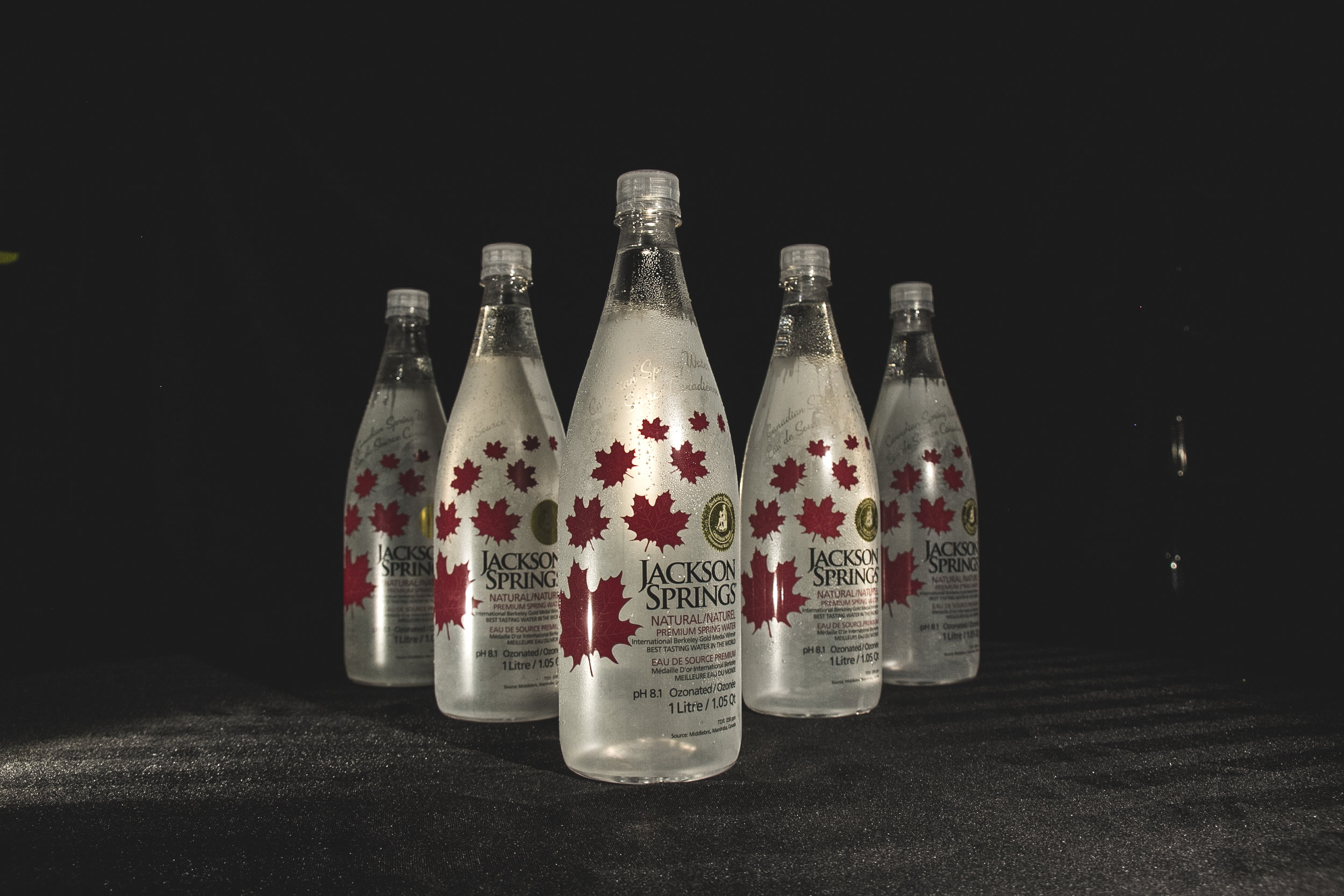 Five bottles of Jackson Springs natural spring water arranged on a dark surface against a black background.